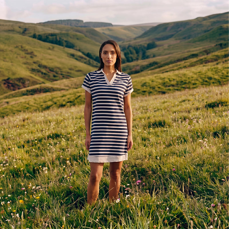 Woman in a striped dress standing in a grassy field with rolling hills in the background